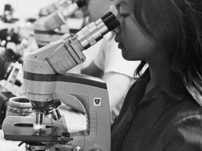Young woman looking through a microscope in a lab.